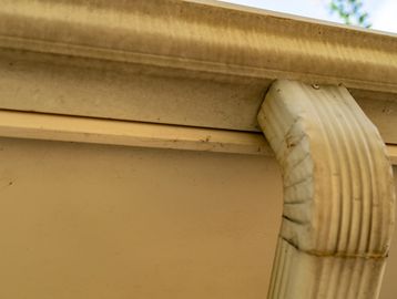 Close-up of a dirty rain gutter and downspout on a beige house.