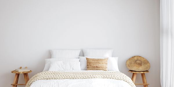 Minimalist bedroom with wooden stools and white bedding.