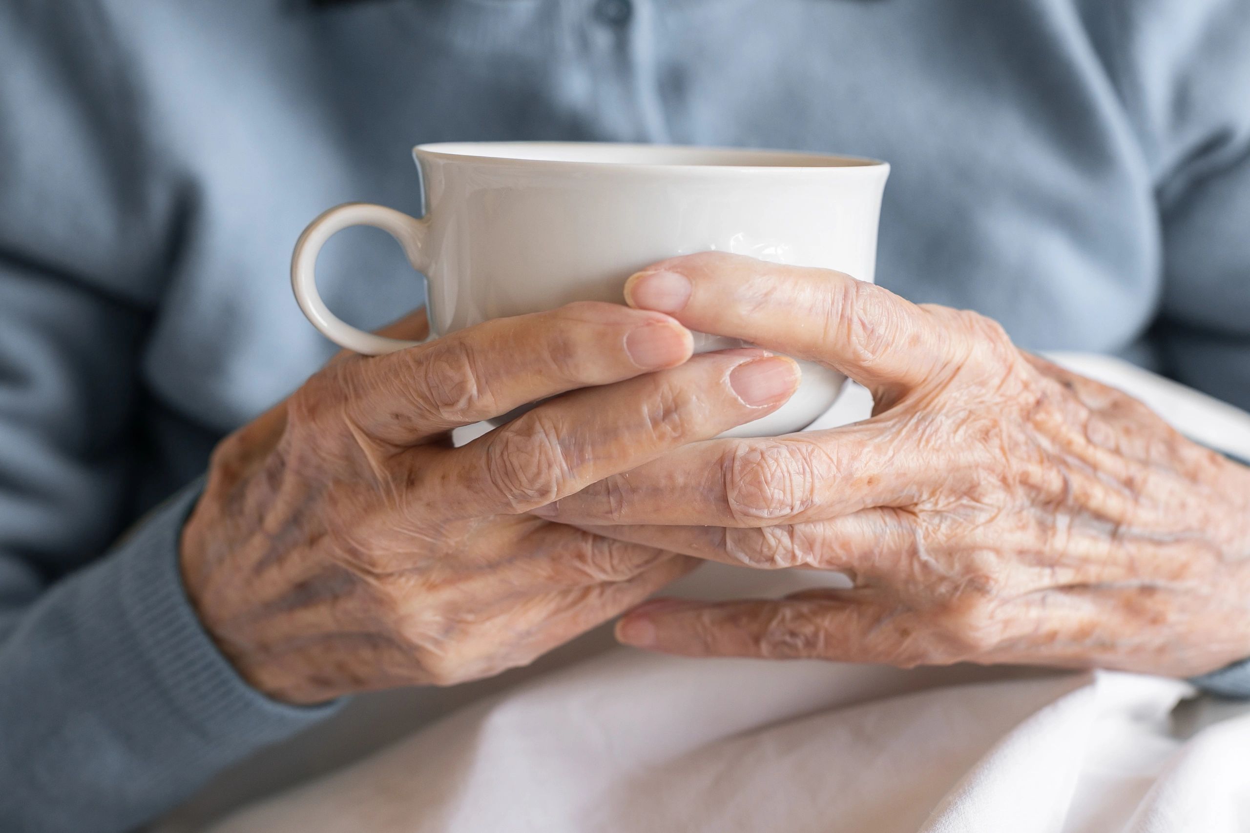 Elderly hands holding a white cup gently.