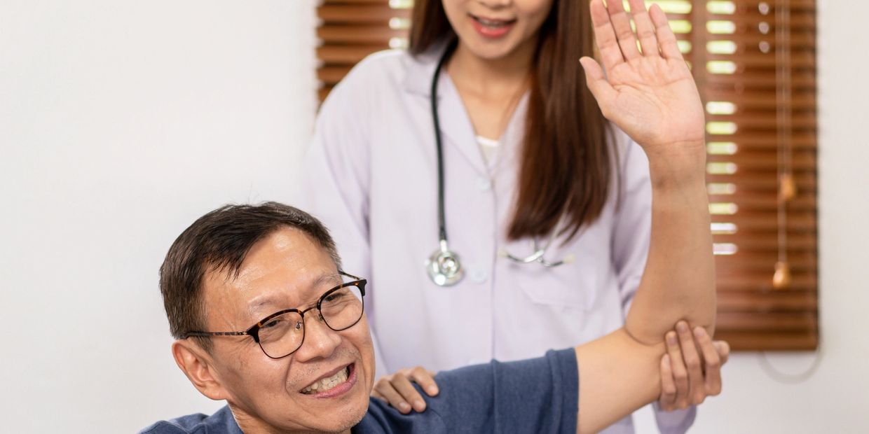 Doctor assisting elderly man with arm exercise in a medical setting.