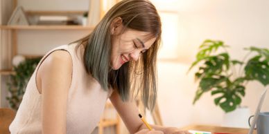 A young woman happily writing at her desk in a cozy room.
