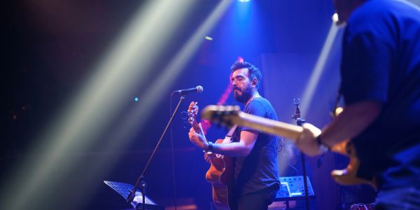 Musician playing guitar on stage with dramatic lighting.