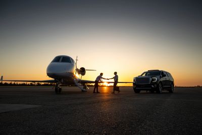 Two men shaking hands near a private jet and SUV at sunset.