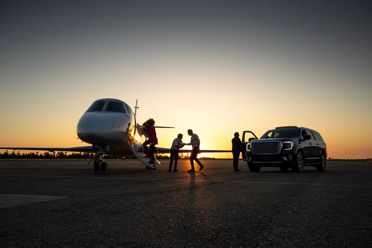 People disembarking a private jet at sunset near a luxury SUV.