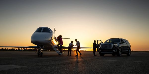 People boarding a private jet at sunset with an SUV nearby.