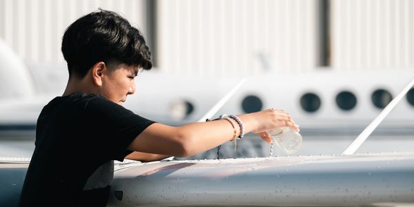 Person cleaning the wing of a small airplane with a cloth.