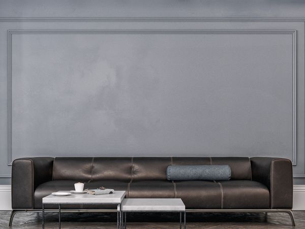 A sleek black leather sofa with a gray bolster pillow against a textured gray wall.