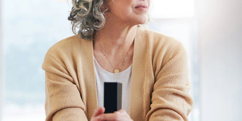 Older woman holding a TV remote, looking thoughtfully.