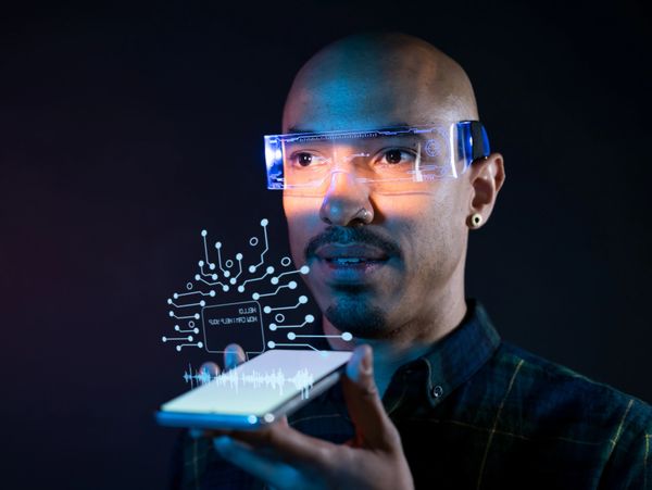 Man wearing smart glasses interacting with a holographic circuit from a smartphone.