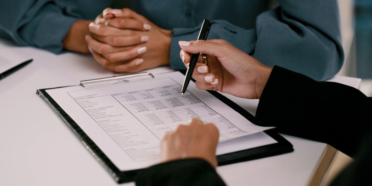 Two people reviewing a financial document on a clipboard during a meeting.