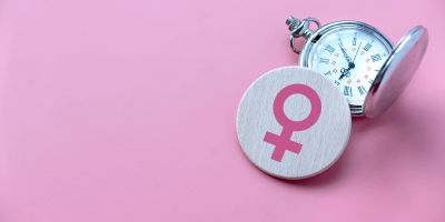 Pocket watch and female gender symbol on pink background.