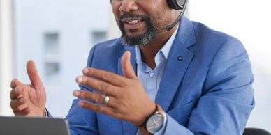 Man in blue suit using headset and laptop for video call.