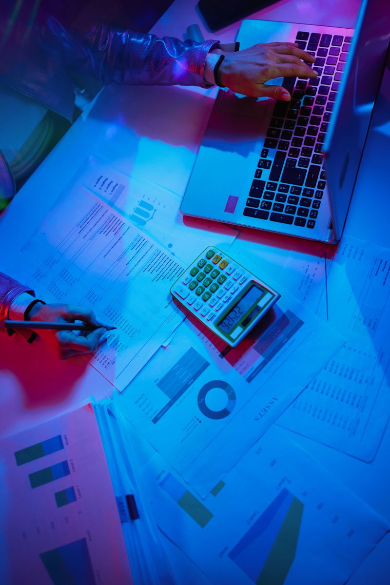 Upper view of modern female with calculator, documents and laptop exploring graphs.