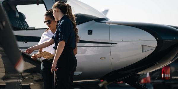 Two women discussing flight plans beside a small airplane on a sunny day.