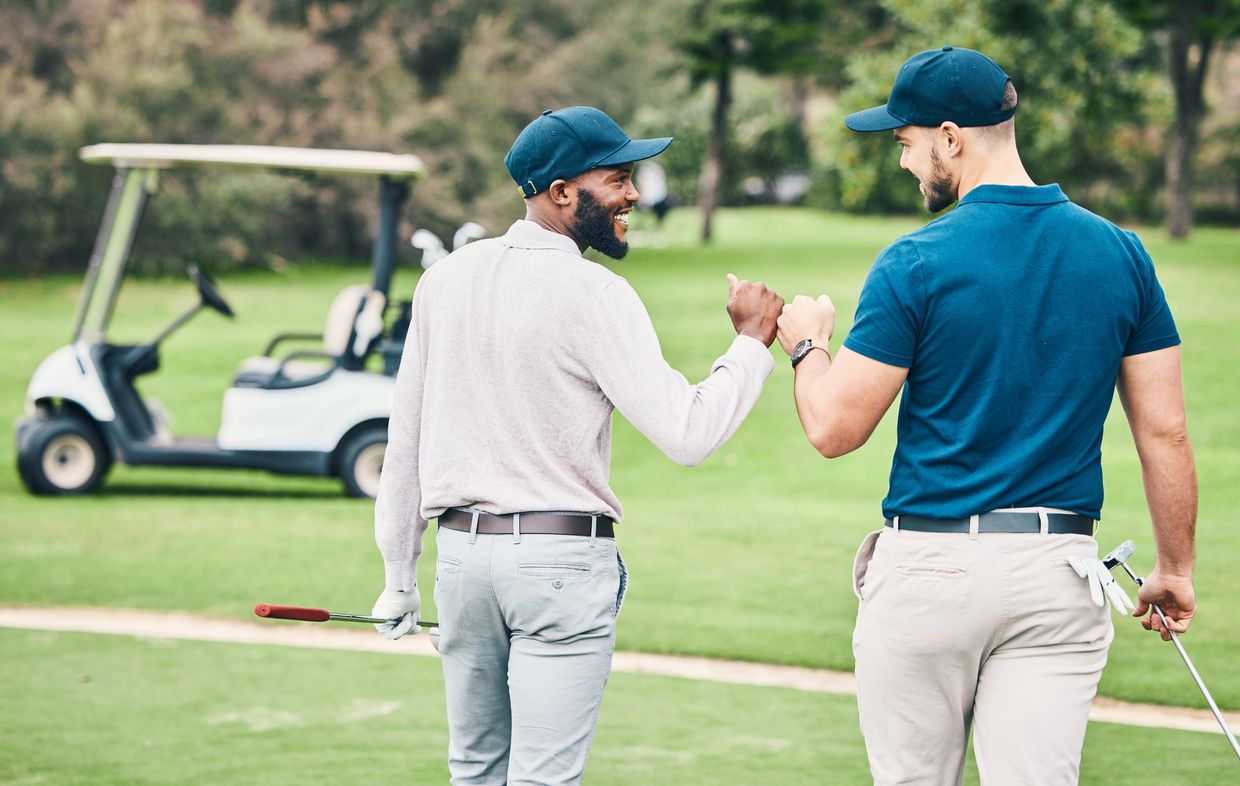 Two men fist bump on a golf course with a golf cart in the background.