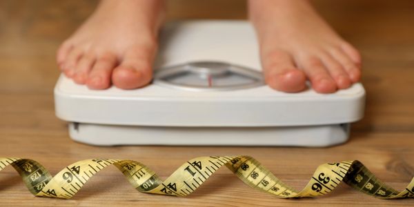 Person standing on a scale with a measuring tape in front.