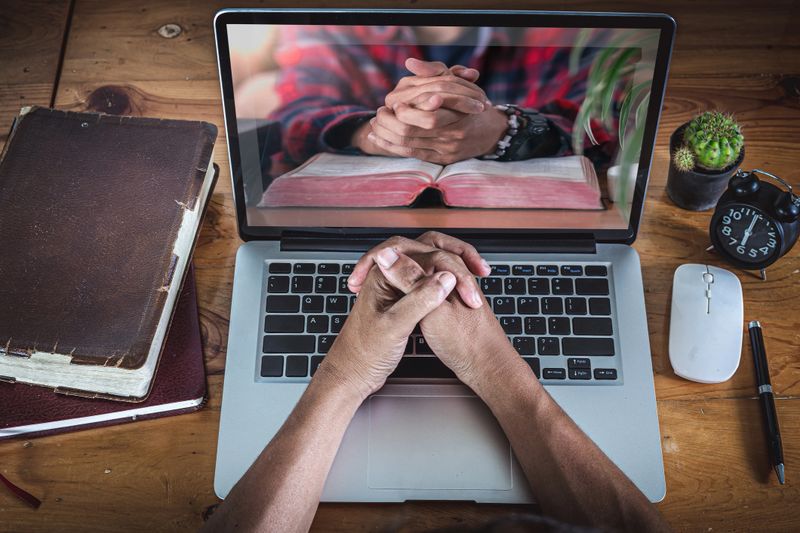 Hands praying on computer laptop, Online church for cell group, Home church during quarantine coronavirus Covid-19, Religion concept