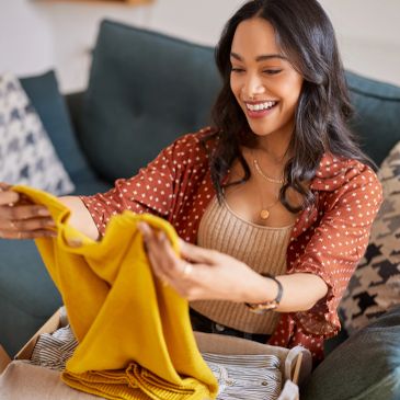 Woman happily folding yellow clothes on a couch.