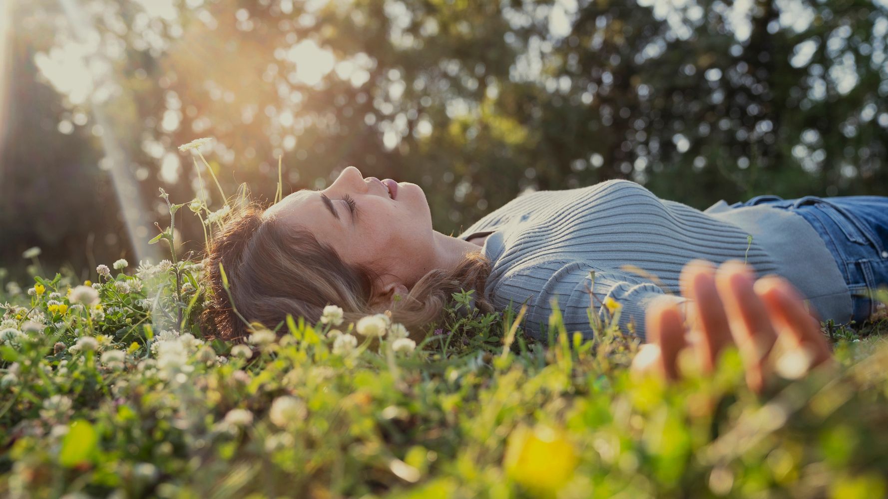 Woman lying peacefully in the grass, eyes closed, enjoying a calm moment of grounding and rest