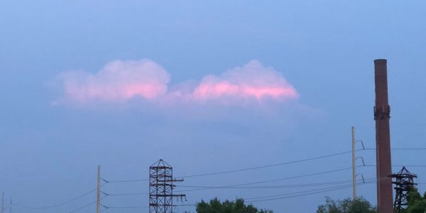Pink clouds glowing softly above industrial structures at dusk.