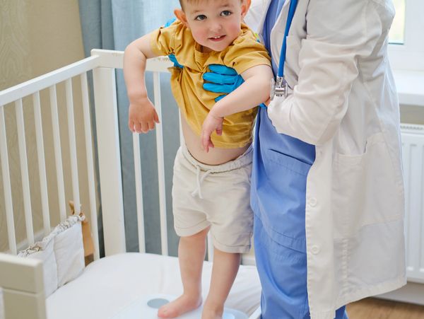 Doctor examining a young boy standing in a crib.