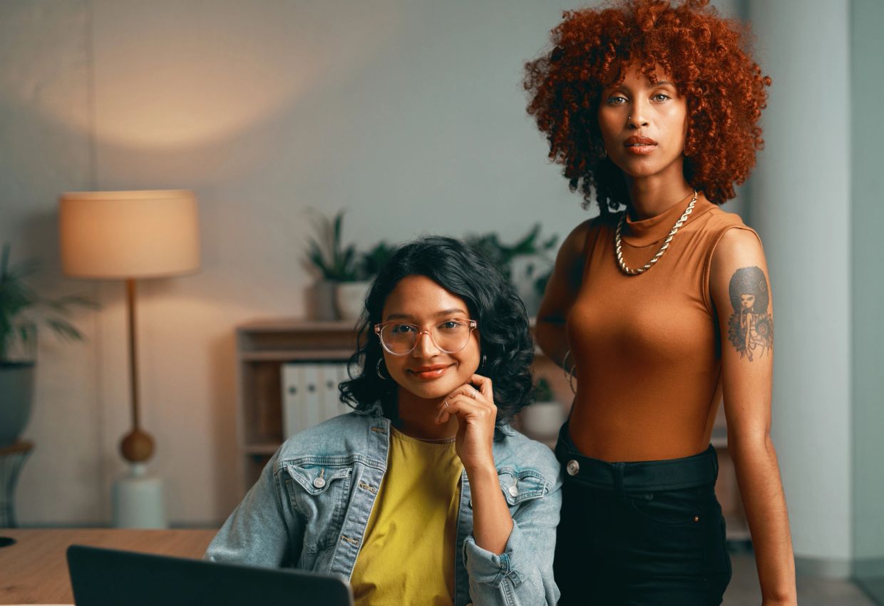 Two confident women posing in a cozy office.
