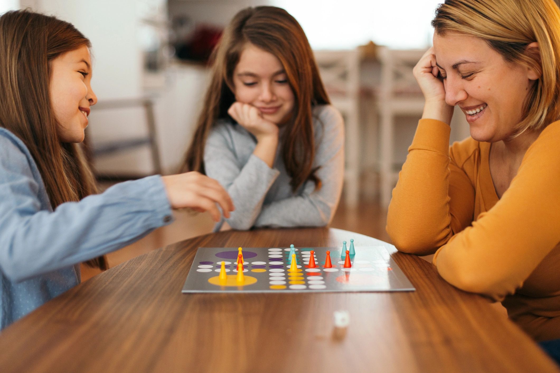 Three females enjoying a board game together at a wooden table.