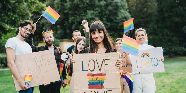 Diverse group holding LGBTQ+ pride signs and rainbow flags outdoors.