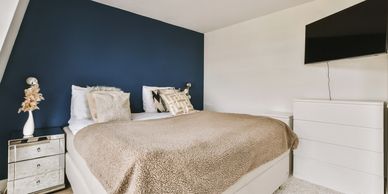 Cozy bedroom with blue accent wall and beige bedding.