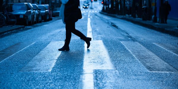 Person crossing a street at a crosswalk during twilight.