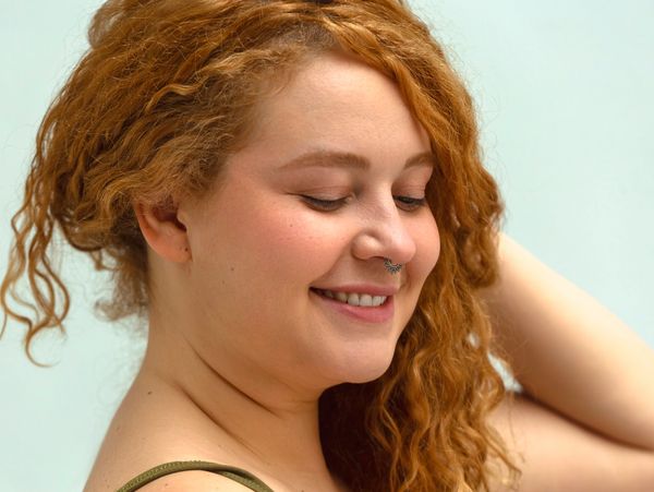 Smiling woman with curly red hair and septum piercing.