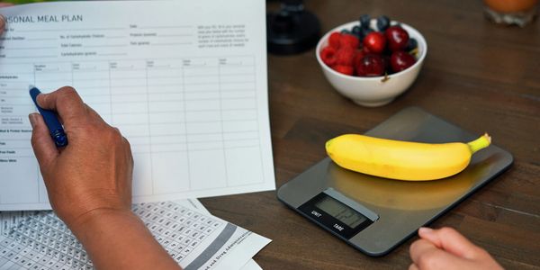 Person filling out a meal plan while weighing a banana on a digital scale.