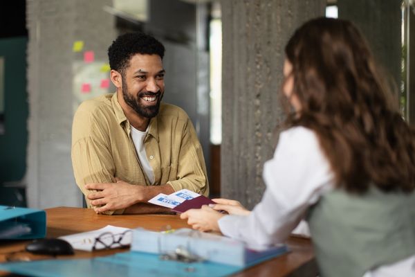 Man smiling while talking to a woman holding travel documents.