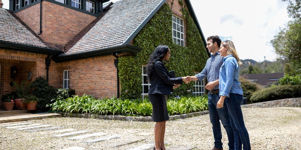 A real estate agent shaking hands with a couple outside a charming brick house.