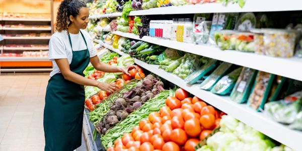 Woman arranging vegetables in a grocery store.