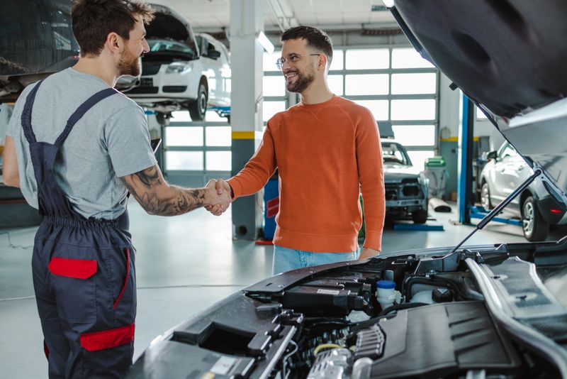 Automotive technicians shaking hands with satisfied customer in garage. Automobile service center worker shaking hands with client after car servicing.