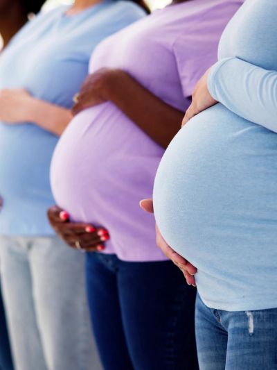 Three pregnant women standing side by side, holding their baby bumps.