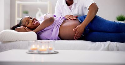 Pregnant woman lying down with a healthcare professional touching her belly.