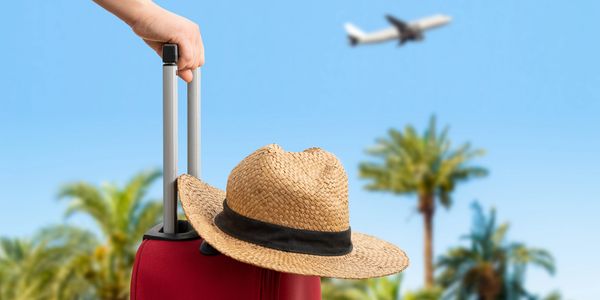 Hat on suitcase with airplane flying in the distance