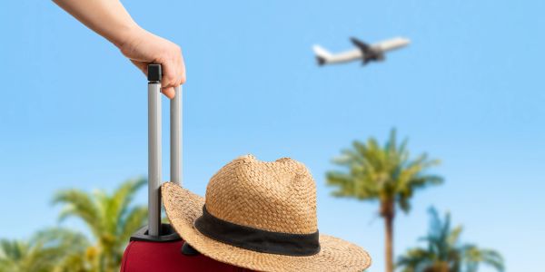 Person holding a suitcase with a hat watching a plane fly by.