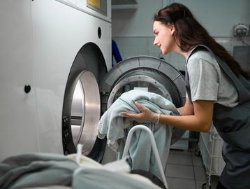 Woman loading clothes into a washing machine in a laundry room.