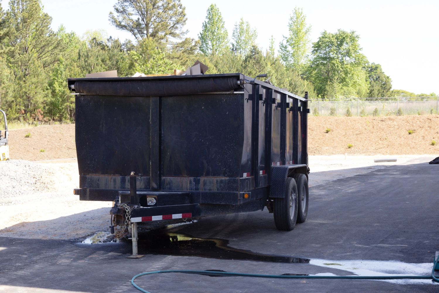 Large black trailer parked outdoors with trees and construction materials.