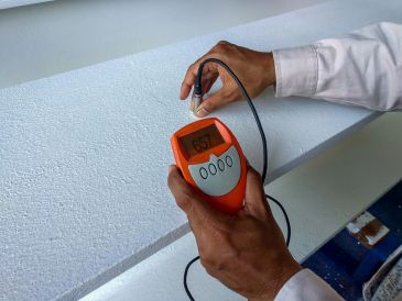 Person measuring material with an orange handheld device.