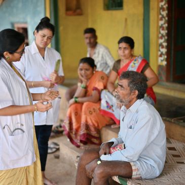 Medical professionals interacting with a seated elderly man in a rural setting.