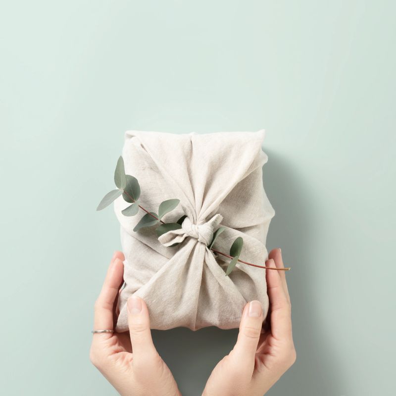 Furoshiki tissue wrapping of presents. Female hand holding a gift in eco friendly reusable fabric package. Small business, ethical shopping idea. Presents packed in plastic free. Zero waste lifestyle