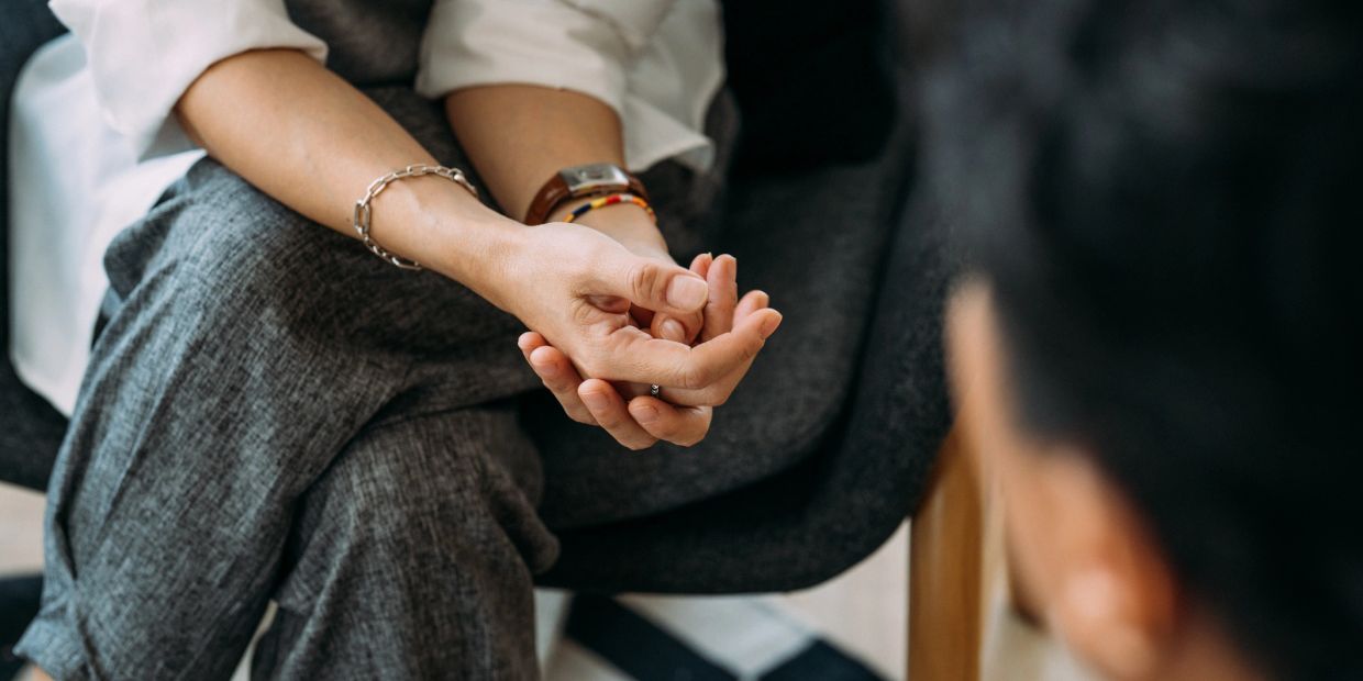 Person sitting with hands clasped, showing nervousness or contemplation.