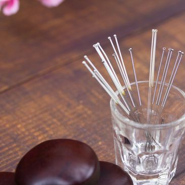 Acupuncture needles in a glass cup on a wooden table.