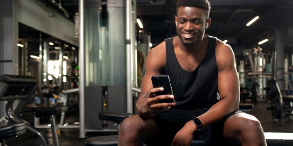 A man in workout clothes smiling at his phone in a gym.