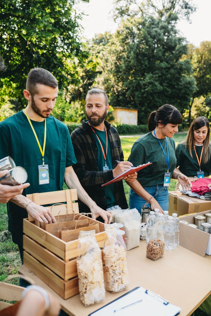 Volunteers are working together at the food and clothes bank. They are wearing badges and green t-shirts. Teamwork of people working on humanitarian aid project.
