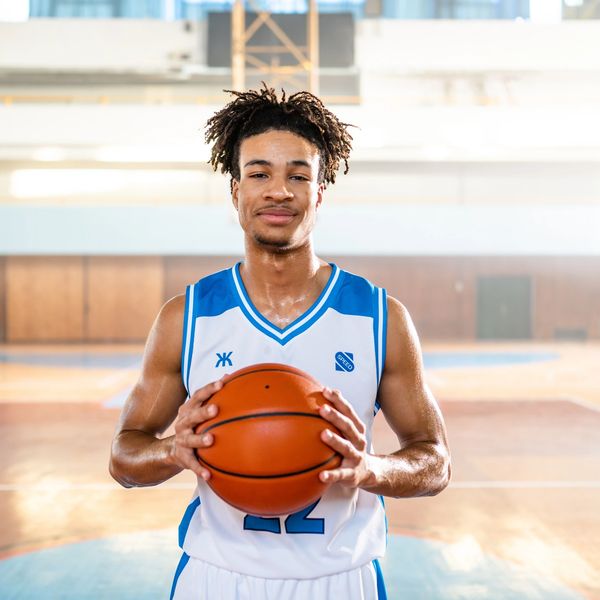 A basketball player holding a ball on an indoor court, smiling confidently.
